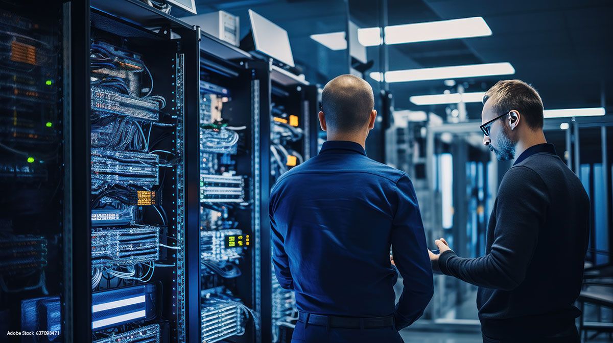 Zwei Männer stehen in einem dunkelblauen Serverraum