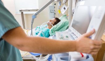 Beatmeter Patient im Krankenbett, Pflegekraft im Vordergrund bedient ein medizinisches Gerät